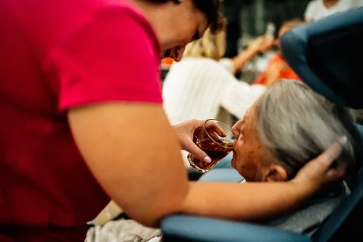 A caregiver helps an elderly woman drink tea, showcasing empathy and support.