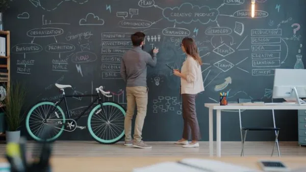 Two professionals collaborate on a chalkboard brainstorming session in a stylish office.