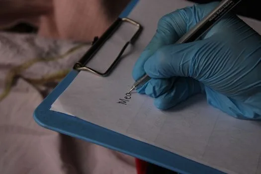 Gloved hand writing in medical setting, pen on clipboard.