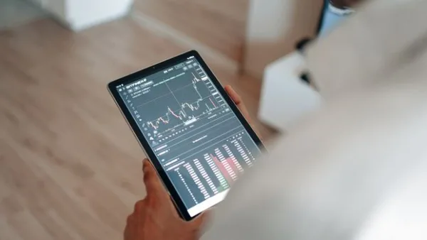 Close-up of person using a tablet displaying trading graphs indoors.