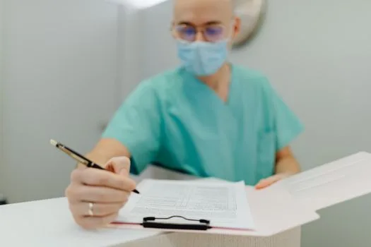 Medical practitioner wearing mask writes notes on clipboard, emphasizing patient care and safety.
