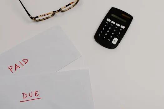 Top view of financial papers labeled 'Paid' and 'Due' beside a calculator and glasses.