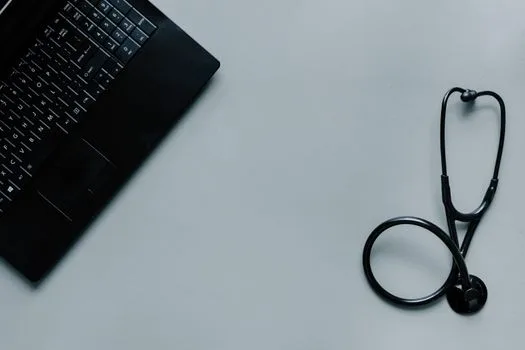 Minimalist image depicting a laptop and stethoscope representing telemedicine and digital health.